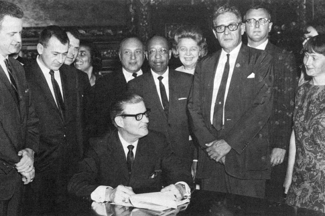 Governor Harold Levander, seated, signs the Minnesota State Act Against Discrimination into law in 1967. It was renamed the Minnesota Human Rights Act in 1973.