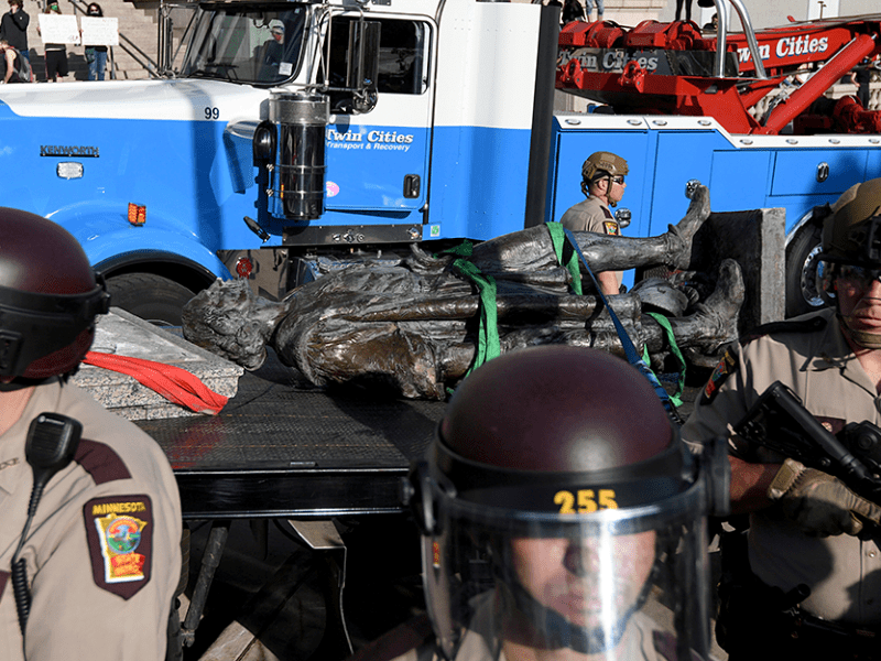 State Patrol officers stand guard as employees of Twin Cities Transport and Recovery work to clear the toppled statue of Christopher Columbus on June 10, 2020.