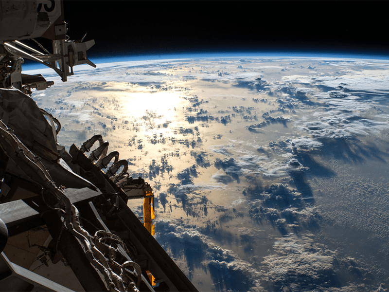 The sun's glint reflects off the Pacific Ocean shadowed by a line of cumulonimbus clouds as the International Space Station orbits about 253 miles above the Earth's surface.