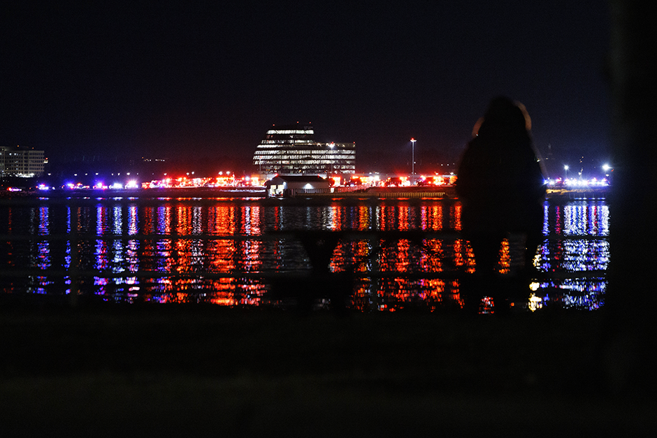 A person watches as crews search for survivors in the Potomac River outside Washington Reagan National Airport on Wednesday where a military Blackhawk helicopter collided with a small plane as it was landing, causing both to crash.